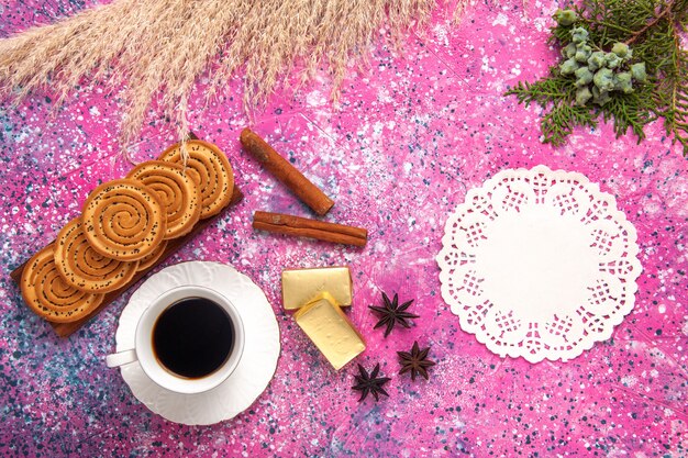 Вид сверху чашка чая с печеньем и корицей на светло-розовом столе.