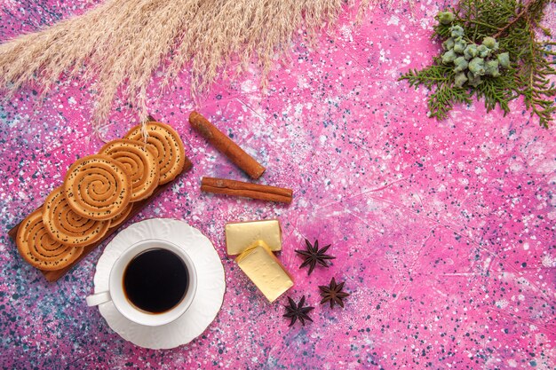 Top view cup of tea with cookies and cinnamon on the light-pink desk.