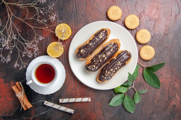 Top view cup of tea with cookies and eclairs on dark table sugar tea biscuit sweets