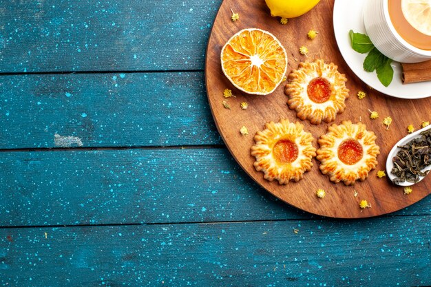 Top view cup of tea with cookies and lemon on the blue desk