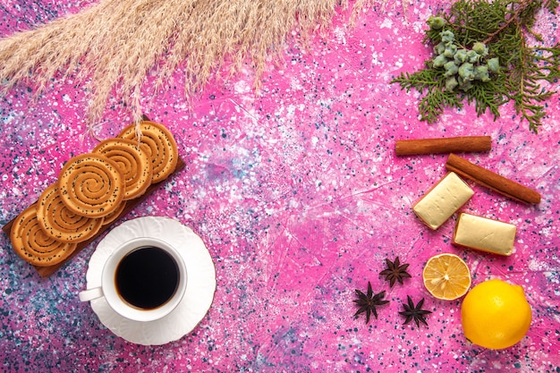 Top view cup of tea with cookies lemon and cinnamon on light-pink desk.