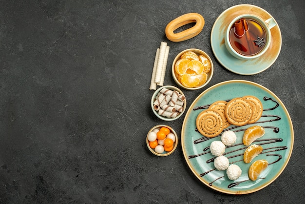 Top view cup of tea with cookies and tangerines on dark background