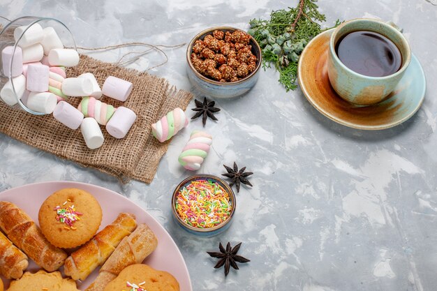 Top view cup of tea with delicious little marshmallows and cakes on the white desk