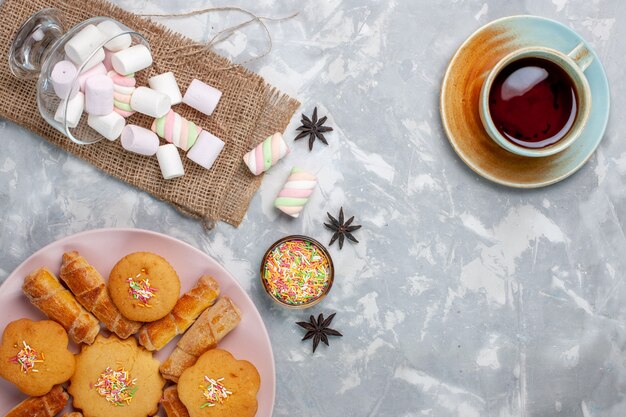 Top view cup of tea with delicious little marshmallows and cakes on white desk