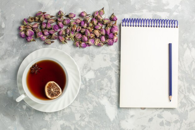 Top view cup of tea with dried little flowers and notepad on the light-white desk