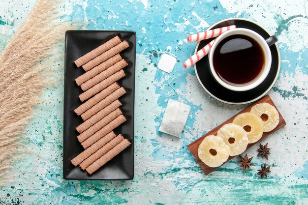 Top view cup of tea with dried pineapple rings and cookies on blue desk