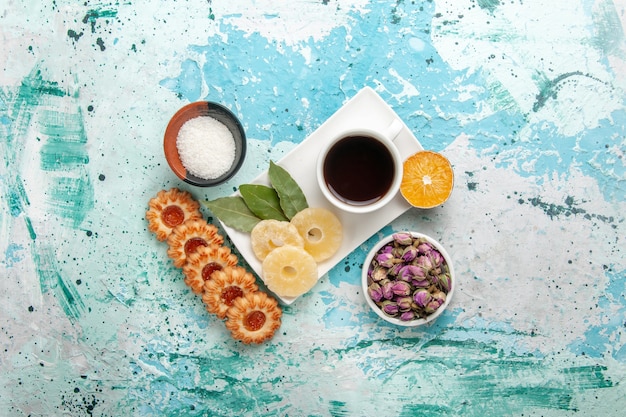 Top view cup of tea with dried pineapple rings and cookies on the light blue surface