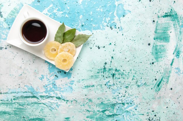 Top view cup of tea with dried pineapple rings on light blue surface