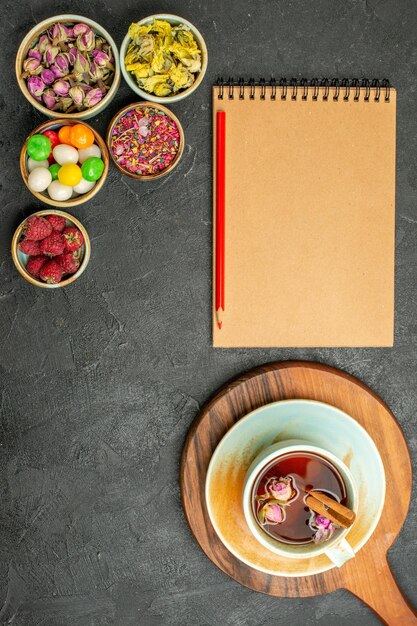 Top view cup of tea with flowers and candies on a grey space