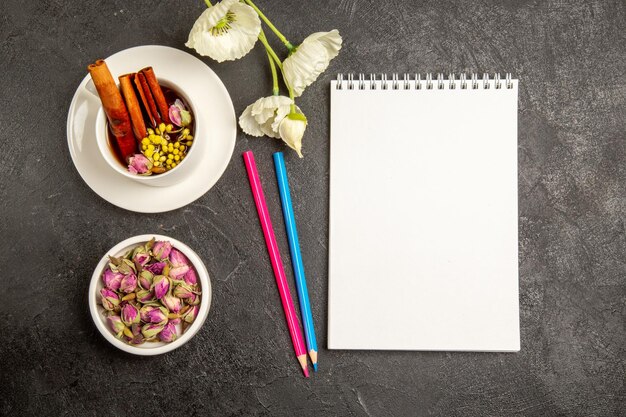 Top view cup of tea with flowers and pencils on grey background tea drink color flower flavor