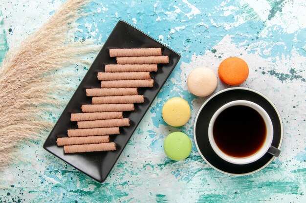 Top view cup of tea with french macarons and cookies on blue surface