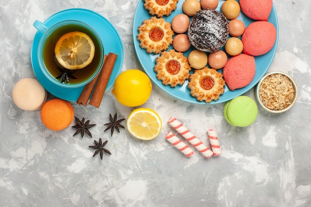 Top view cup of tea with french macarons cookies and cakes on the white surface