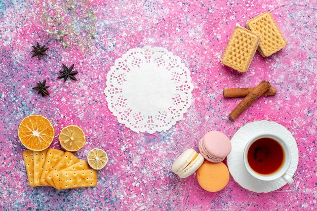 Foto gratuita vista dall'alto tazza di tè con macarons francesi e cracker sulla scrivania rosa chiaro