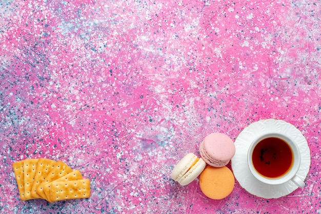 Top view cup of tea with french macarons and crackers on the pink desk