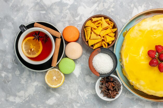 Top view cup of tea with french macarons and delicious yellow syrup cake on white surface