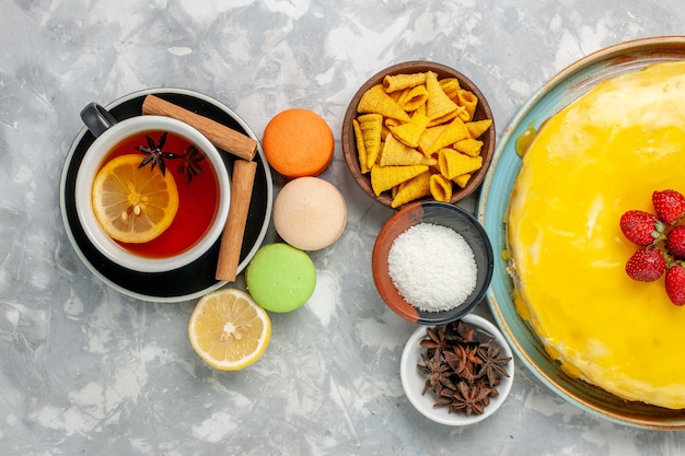 Top view cup of tea with french macarons and delicious yellow syrup cake on white surface