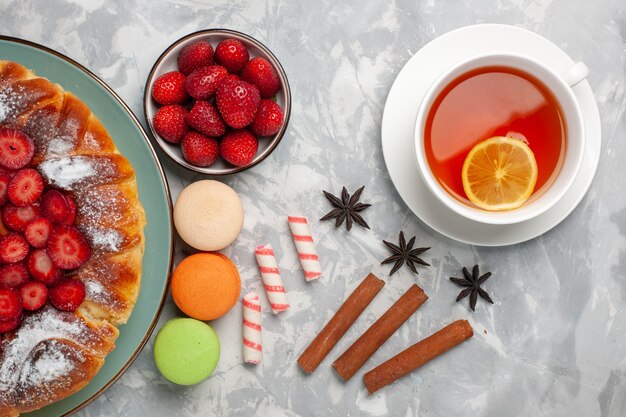 Top view cup of tea with french macarons and pie on light white surface