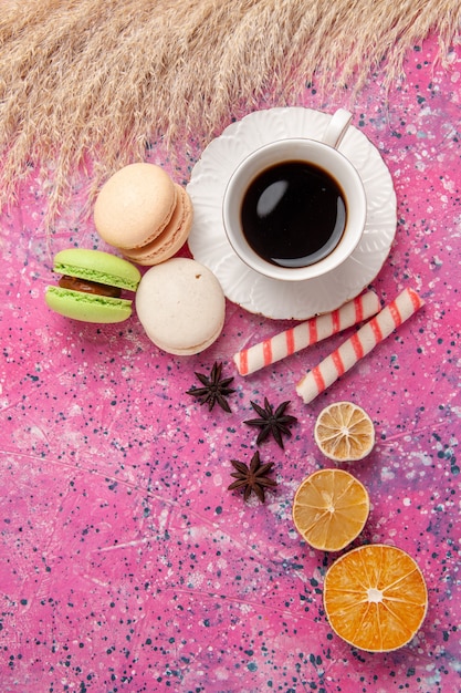 Вид сверху чашка чая с французскими макаронами на розовом столе, печенье, сладкий сахарный пирог