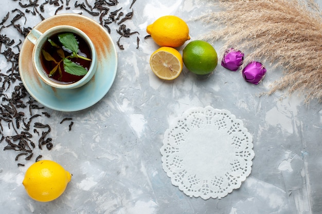 Top view cup of tea with fresh dried tea grains candies and lemon on the light table, tea drink breakfast