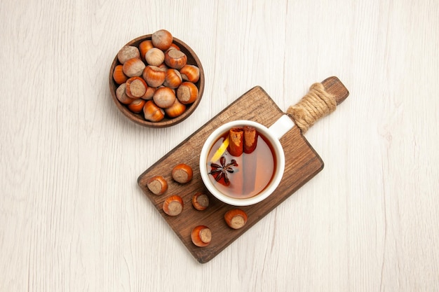 Top view cup of tea with fresh hazelnuts on white surface tea nut snack ceremony