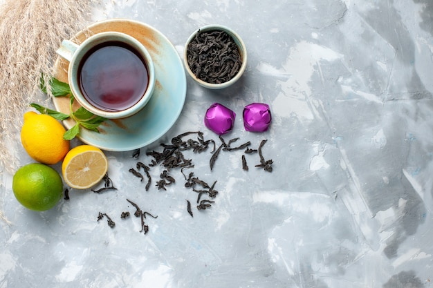 Top view cup of tea with fresh lemons candies and dried tea on white table, fruit citrus color