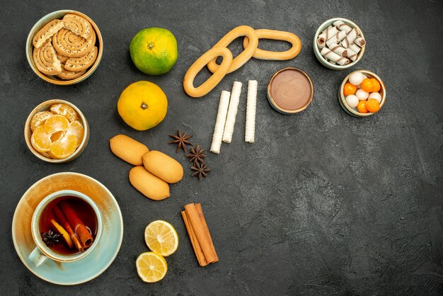 Top view cup of tea with fruits and biscuits on the dark background