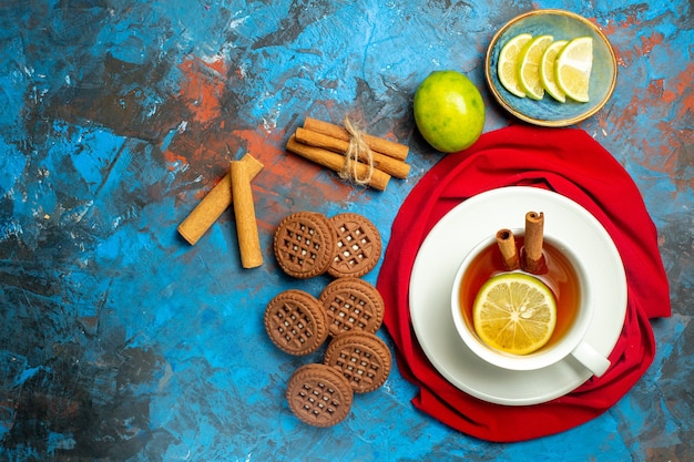 Top view cup of tea with lemon and cinnamon red shawl on blue red surface with copy place