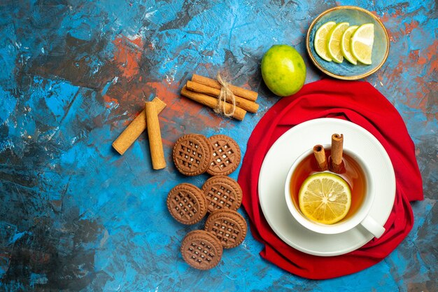 Top view cup of tea with lemon and cinnamon red shawl on blue red surface with copy place