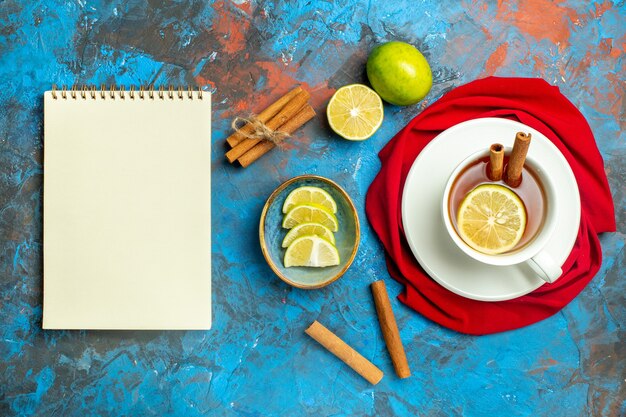 Top view cup of tea with lemon and cinnamon red shawl notepad on blue red surface