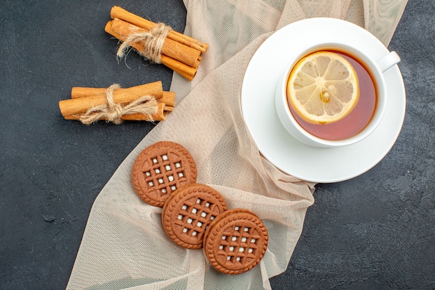 Foto gratuita vista dall'alto una tazza di tè con biscotti al limone e bastoncini di cannella su scialle beige su superficie scura