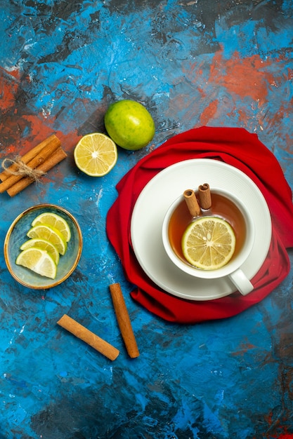 Вид сверху чашка чая с лимоном и палочками корицы красный шаль на сине-красной поверхности