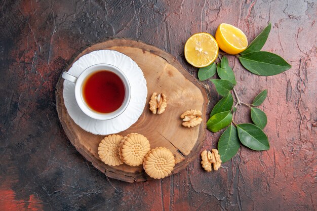 Top view cup of tea with lemon and cookies on dark table sweet biscuit cakes