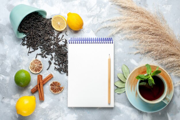 レモンのドライティーとシナモンのメモ帳をライトテーブル、穀物茶乾燥色の柑橘系の果物とお茶の上から見るカップ