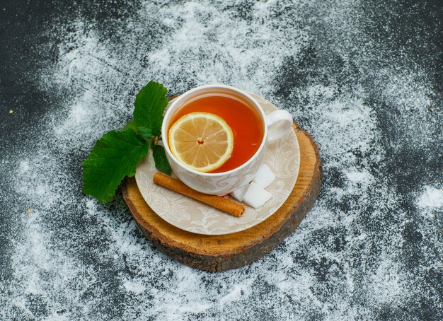 Top view a cup of tea with lemon, dry cinnamon, sugar cubes on wood slices and dark. horizontal