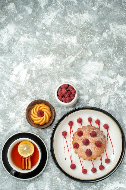 Top view a cup of tea with lemon slices and cinnamon berry cake on oval plate on grey surface copy place