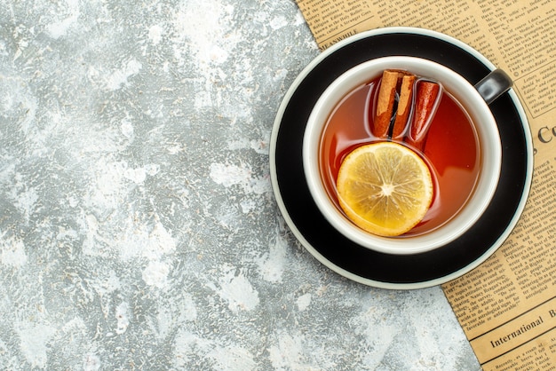 Foto gratuita vista dall'alto una tazza di tè con fette di limone e bastoncini di cannella sul giornale sul posto di copia superficie grigia