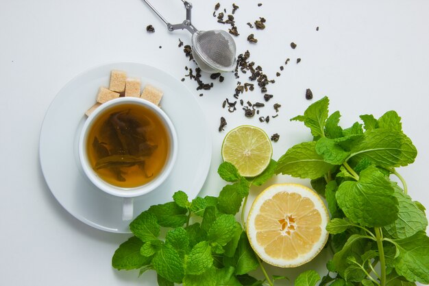 Top view a cup of tea with lemon, sugar, mint leaves on white surface. horizontal