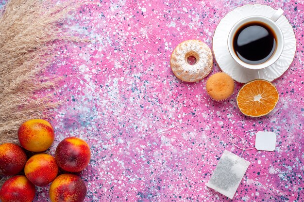 분홍색 표면에 작은 케이크와 신선한 복숭아와 차 한잔의 상위 뷰