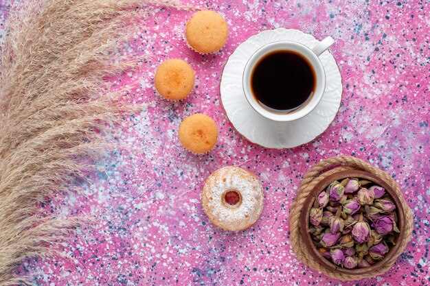 Top view of cup of tea with little cakes on pink surface