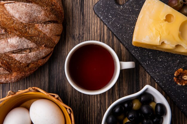 Top view cup of tea with maasdam cheese on a stand with olives and black bread on the table