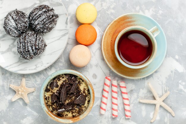 Top view cup of tea with macarons chocolate cakes and candies on white desk bake cake biscuit sugar sweet pie