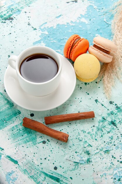 Top view cup of tea with macarons and cinnamon on blue surface