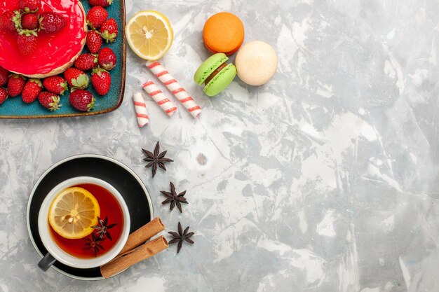 Top view cup of tea with macarons and little strawberry cake on the white surface