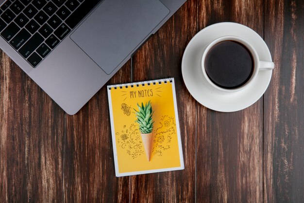 Top view cup of tea with notepad and laptop on wooden background