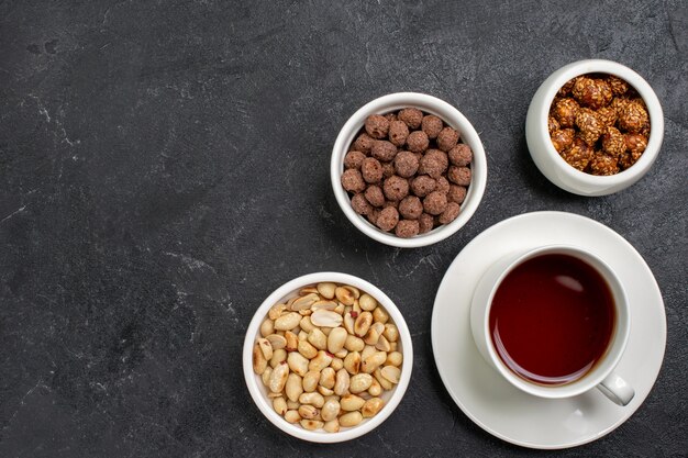 Top view cup of tea with nuts and candies on dark-grey space
