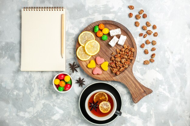 Top view cup of tea with nuts and candies on white wall candy sugar sweet cookie cake tea