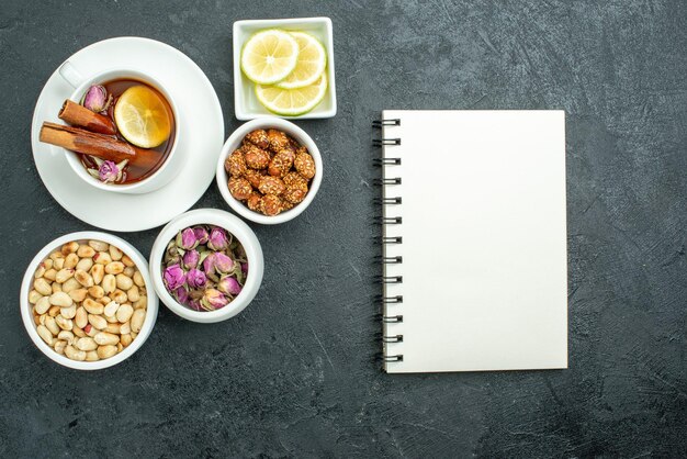 Top view cup of tea with nuts notepad and candies on dark surface tea ceremony nut candy