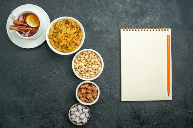 Top view cup of tea with nuts and raisins on dark surface snack nut sweet tea