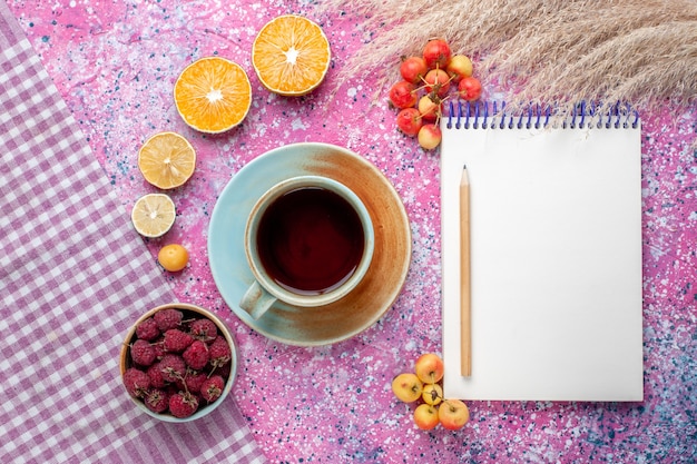 Top view of cup of tea with orange slices and raspberries on pink surface