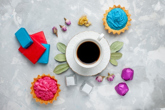 Top view of cup of tea with pink cream cake chocolate candies on light desk, biscuit sweet tea candy